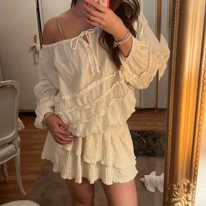 Krämvit volang tröja  i bomull - Supersöt krämvit tröja med volanger och smockad struktur.  Har en luftig känsla och är perfekt för varma dagar. Tillverkad i bomull och har en lätt, flowy passform som ger en romantisk vibe.