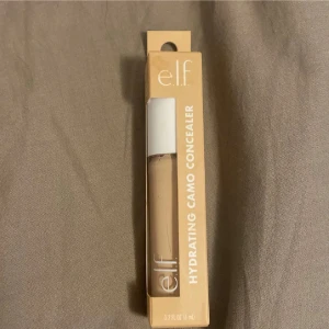 e.l.f. Hydrating Camo Concealer Fair Beige - e.l.f. Hydrating Camo Concealer i nyansen Fair Beige. Kommer i en beige förpackning med vit kork och har en oversized applikator för enkel applicering. Ger en återfuktande finish och passar för att täcka, skulptera och highlighta.