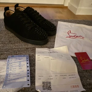 Christian Louboutin svarta sneakers med nitar - Pris kan diskuteras! Aldrig använda! Allt i bilden ingår. Svarta sneakers från Christian Louboutin i mocka med ikonisk röd sula och svarta nitar på tån. Skorna har snörning och rund tå, samt exklusiv känsla med märkets logga på innersulan. Perfekta för dig som vill sticka ut med edgy detaljer.