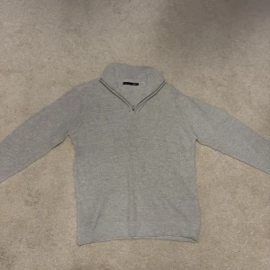 Ljusgrå stickad tröja med half zip - Säljer en ljusgrå stickad tröja från Selected Homme med half zip och hög krage. Tröjan har lång ärm och är perfekt för lager-på-lager. Enkel och stilren design som passar till det mesta.