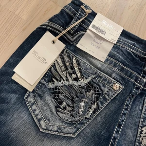 Miss Me Curvy Boot jeans med broderi - Snygga Miss Me Curvy Boot jeans i mörkblå tvätt med coolt broderi och detaljerade nitar på bakfickorna. Bootcut-modell med kontrastsömmar och slitningar för en edgy look. Perfekt för dig som gillar statement-jeans med extra attityd. helt nya m prislapp köpta i butik i usa