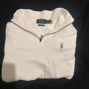 Vit half zip tröja från Polo Ralph Lauren - Säljer en äkta finnsbevis, Snygg vit tröja från Polo Ralph Lauren med half zip och klassisk broderad logga på bröstet. Tillverkad i mjuk bomull, perfekt för chill dagar. Tröjan har en stilren design med ståkrage och ribbade muddar. Passar dig som gillar clean och tidlös stil.