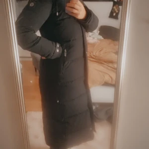 Vinterjacka HOLLIES  - Säljer en svart lång dunjacka med stor fluffig päls på luvan. Jackan har dragkedja och knappar framtill, samt fickor på sidorna. Perfekt för kalla dagar med sin varma och stilrena look. Luvan är riktigt maffig och ger jackan en cool vibe. Märket är hollies och har köpts förra vintern i Barkaby hollies Stockholm. Nypriset var 4999 kr säljes nu för 1500 kr. Priset går att diskutera såklart 🥰 