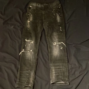 Supply and demand slim fit jeans - Svarta jeans med coolt slitna partier och trasiga knän, samt små vita färgstänk och nitar som ger en edgy vibe. Modellen är rak med normal passform och klassiska fem fickor. Perfekt för dig som gillar streetstyle och vill sticka ut.