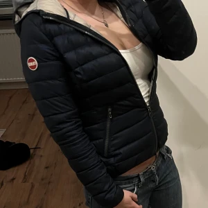Mörkblå Colmar pufferjacka med huva - Storlek 42 vilket passar typ xs/s! Snygg mörkblå pufferjacka från Colmar med huva och ljusgrått foder. Jackan har två dragkedjeförsedda fickor, Colmar-logga på ärmen och quiltad design. Perfekt för kalla dagar och har en slim passform som sitter riktigt nice.