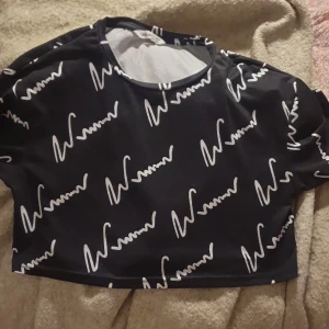Svart croppad topp med vitt mönster från SHEIN - Cool croppad topp från SHEIN i svart med vitt grafiskt mönster. Rund halsringning och korta ärmar. Materialet är mjukt och stretchigt, troligen polyester. Perfekt för dig som gillar streetstyle och vill sticka ut med ett unikt print.