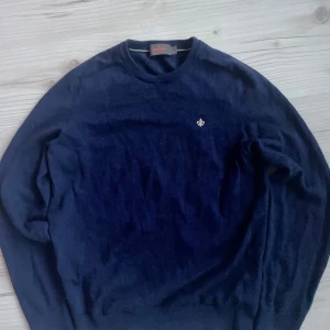 Mörkblå merinoullströja från Morris - Snygg mörkblå stickad tröja från Morris i mjuk merinoull. Klassisk rund halsringning och diskret broderad logga på bröstet. Perfekt för dig som gillar stilrena och tidlösa plagg med en clean look.