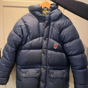 Mörkblå fjällrävenjacka - Säljer den här jättevarma vinterjackan ifrån Fjällräven. Vet inte exakt modell då det inte står men den är lite tjockare än expetidion down lite, men jag tror det är för att detta är en äldre modell. Den har ett litet hål där fram men det borde gå att laga. 