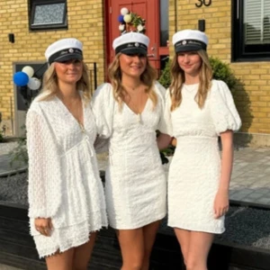 Vit kort studentklänning  - Superfin vit kort klänning med v-ringning, långa ärmar och volangdetaljer. Klänningen har struktur i tyget och knyt i midjan för en snygg passform. Perfekt för student eller sommarens alla tillfällen!