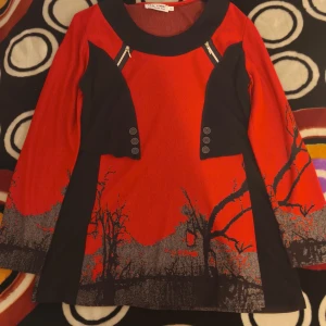 Röd och svart kortklänning med tryck - Unik röd och svart kortklänning från New York med coolt grafiskt tryck av träd i grått och svart nedtill. Klänningen har långa ärmar, bred svart krage, dekorativa knappar och dragkedjor vid axlarna. Materialet känns mjukt och stretchigt, perfekt för dig som gillar statement-plagg.