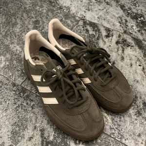 Adidas Handball Spezial sneakers grön/vit - Säljer ett par Adidas Handball Spezial sneakers i grön mocka med klassiska vita ränder och vit Snygg retrostil med bruna gummisulor och snörning. Perfekta för dig som gillar streetwear och vill ha en ikonisk sneaker i garderoben. Använda en gång