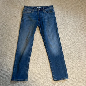 Blå jeans från Jack & Jones - Snygga blå jeans från Jack & Jones med klassisk femficksdesign och raka ben. Jeansen har en normal passform och är tillverkade i slitstarkt denimtyg med snygga slitningar och kontrastsömmar. Perfekta för en avslappnad och trendig look.