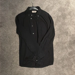 Svart skjorta Tiger of Sweden Jeans - Svart långärmad skjorta från Tiger of Sweden Jeans i klassisk modell med knappar framtill och bröstficka. Skjortan har button down-krage och stilren look.