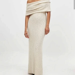 Lång ribbad offshoulder klänning - Superfin långklänning i ljusbeige ton med ribbad struktur och offshoulder-design. Klänningen har en figurnära passform och bred krage som vilar snyggt över axlarna. Perfekt för dig som vill ha en elegant och stilren look.