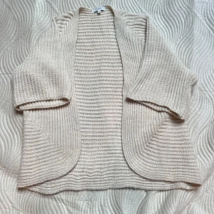 Beige stickad kofta från Sorbet - Mysig beige stickad kofta från Sorbet i storlek S/M. Koftan har ett öppet och avslappnat snitt med trekvartsärmar och ribbad struktur. 