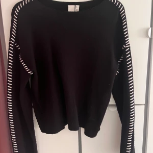 Svart stickad tröja - Svart stickad tröja från Y.A.S i storlek XS. Tröjan har lång ärm och coola vita detaljer längs axlar och ärmar som ger en unik look. Perfekt för dig som gillar stilrena plagg med en twist. Rund hals och mjukt material.