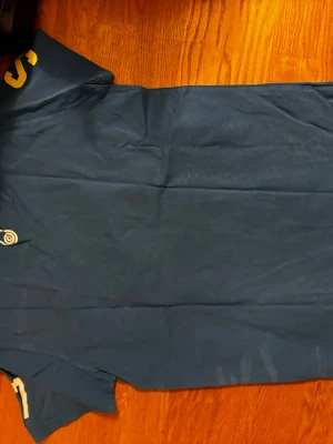 Blå t-shirt från Sail Racing - Säljer en blå t-shirt från Sail Racing med tryckta bokstäver i gult och vitt på ärmarna samt en rund logotyp på bröstet. T-shirten har rund hals och är tillverkad i mjuk bomull. Perfekt för dig som gillar sportig och clean stil.