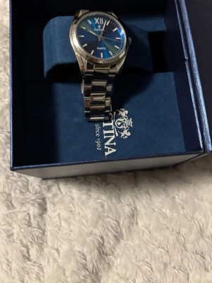 Blå Festina klocka med stållänk - Snygg Festina klocka med blå urtavla och silverfärgad stållänk. Klassisk design med romerska siffror vid tolvslaget och kvartsverk. Klockan kommer i originalask och extra länkbitar medföljer för justering av storlek. Finns också 2 extra länkar till 