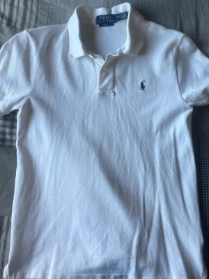Vit piké från Polo Ralph Lauren - Säljer en klassisk vit pikétröja från Polo Ralph Lauren i slim fit-modell. Endast använd 1 gång!