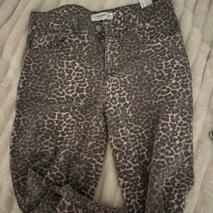 Leopardmönstrade jeans från Pull&Bear - Säljer ett par snygga jeans från Pull&Bear i storlek 34 med leopardmönster. Byxorna har klassisk femficksdesign, knapp och dragkedja framtill samt bälteshällor. Färgen är en mix av beige och mörkbrun, och materialet är jeans med ett coolt djurmönster.