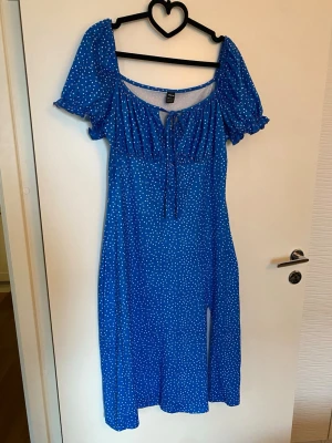Klarblå prickig klänning  - Superfin klarblå klänning med vita prickar från SHEIN. Klänningen har puffiga korta ärmar med volangkant, rundad halsringning och knyt framtill. Längden är mitt på vaden och materialet känns lätt och skönt. Perfekt för dig som gillar färg och mönster!