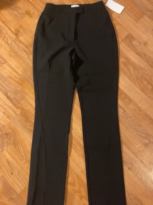 Svarta kostymbyxor från NA-KD, strl 36 - Snygga svarta kostymbyxor från NA-KD med hög midja och raka ben. Byxorna har diskreta fickor bak, dragkedja och knapp framtill. Tillverkade i ett mjukt och hållbart material som känns bekvämt hela dagen.