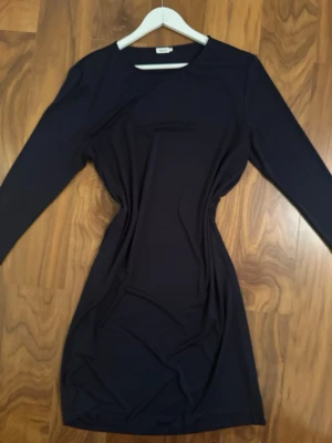 Marinblå klänning  - Snygg marinblå klänning  med långärmade och rund hals. Modellen är figurnära och kort, perfekt för dig som gillar stilrena och enkla plagg. Materialet känns mjukt och stretchigt, vilket gör den bekväm att bära hela dagen.
