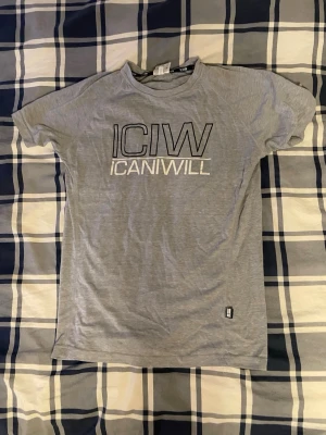 Grå ICANIWILL t-shirt i bomull - Snygg grå t-shirt från ICANIWILL med stor logga framtill. Klassisk rund hals och korta ärmar. Tillverkad i mjuk bomull som känns skön mot huden. Perfekt för dig som gillar enkel och sportig stil.
