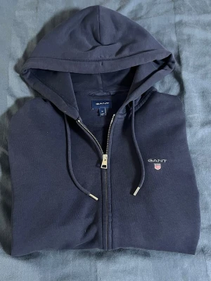 Gant zip hoodie - Säljer min gamla gant zip hoodie. Den har inga hål eller defekter. Den har dock ett litet vitt märke längst ner på tröjan (se bild) men den syns knappt. Storlek MJag har vuxit ur denna tröjan så det är dags att sälja. Om du har några frågor så är det bara att skriva till mig!😀😄