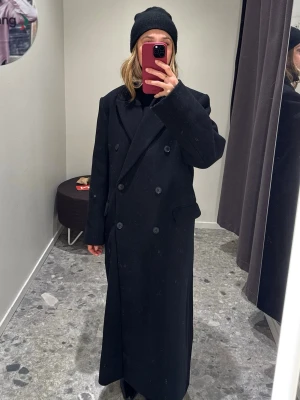 Svart lång Weekday kappa - Säljer en svart lång kappa från Weekday med dubbelknäppning och breda slag. Jackan har två fickor med lock och en rak, oversized passform. Perfekt för dig som gillar minimalistisk stil och vill ha en tidlös jacka. Kappan är använd en gång. Storlek M.