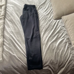 Svarta träningsbyxor från SOC - Svarta träningsbyxor från SOC med resår i midjan och raka ben. Tillverkade i ett syntetmaterial som andas och håller dig torr och bekväm under träning. Funkar bra som ”överdragsbyxor” till t.ex. fotboll. Säljer då de är för små för mig☺️