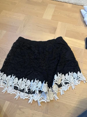 Svarta spets-shorts med vit kant - Snygga svarta shorts med blommig spets och vit broderad kant längst ner. De har elastisk midja och är riktigt sköna att ha på sig. 