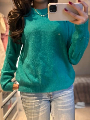 Grön tröja med rund hals - Säljer en grön stickad tröja med rund hals och ribbade muddar vid ärmslut och nederkant. Tröjan har en loose passform och långa ärmar, perfekt att matcha med jeans för en chill look.