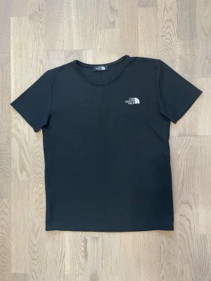 Svart t-shirt från The North Face - Svart t-shirt från The North Face med klassisk rund hals och korta ärmar. Diskret logga i vitt på bröstet. Materialet är bomull och har en lätt ribbad struktur som ger en cool känsla. Fungerar extremt bra till aktiviteter och gymmet! Hör av dig vid intresse, pris kan diskuteras!