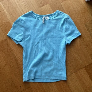 Ljusblå ribbad topp från Divided H&M - En ljusblå ribbad topp från Divided med korta ärmar och rund halsringning. Perfekt att matcha med jeans eller kjol för en fräsch look.