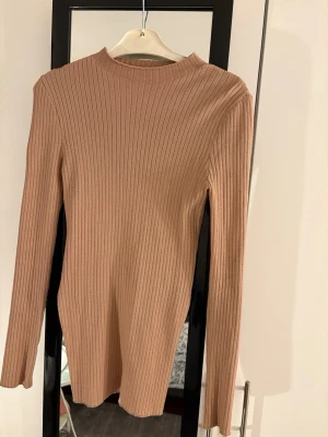 Beige ribbad långärmad tröja - Säljer en beige ribbad långärmad tröja med slits på sidorna. Tröjan har en rundad hals och är tillverkad i ett mjukt stickat material som sitter snyggt på kroppen.