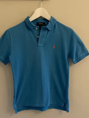 Blå Polo Ralph Lauren t-shirt - Snygg blå t-shirt från Polo Ralph Lauren med klassisk krage och korta ärmar. Säljer då jag har vuxit ur den. Den är i storlek 10-12 år. Bara att fråga om det skulle vara något ni undrar