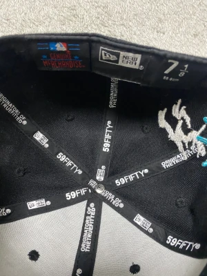 New Era 59FIFTY svart keps New York - Säljer en svart New Era 59FIFTY keps med broderad text 'Greetings from New York' och frihetsgudinnan i turkos och vitt på sidan. Platt skärm i ljus beige och klassisk passform. MLB Genuine Merchandise. Perfekt för dig som gillar streetwear och snygga detaljer.