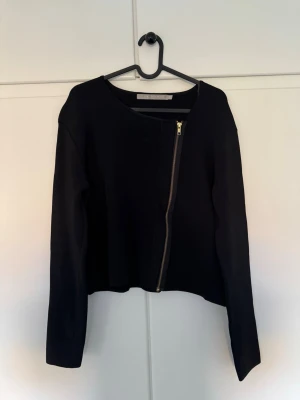 Tiger of Sweden Valere tröja/jacka - Snygg svart jacka från Tiger of Sweden i storlek L. Modellen heter Valere och har en cool sned dragkedja framtill. Jackan är långärmad och har en stilren, minimalistisk look som passar perfekt till jeans eller kjol.