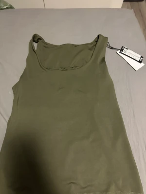 Olivgrön linnetopp från only - Snygg olivgrön linnetopp från only, helt vändbar med rundad halsringning och ärmlös design. Tunn och mjuk polyester som känns skön mot huden. Perfekt för varma dagar och enkel att matcha med jeans eller shorts. Helt nytt med prislapp orinal pris 230kr
