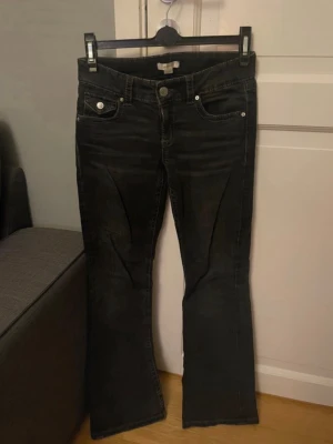 Bootcut svarta jeans från Gina Tricot - Svarta jeans från Gina Tricot i bootcut-modell med klassiska fem fickor och silverfärgade knappar. Jeansen har låg midja och är tillverkade i ett mjukt bomullsmaterial med lite stretch. Perfekta för dig som gillar en retro vibe och vill ha snygga ben.