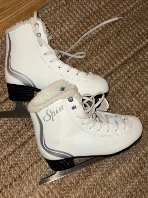 Vita skridskor Spin 36 - Snygga vita konståkningsskridskor från Spin med silvriga detaljer och snörning. Insidan är fodrad med mjukt, ljust foder för extra komfort. Perfekta för isbanan och har en klassisk design med hög ankel och robust klack.