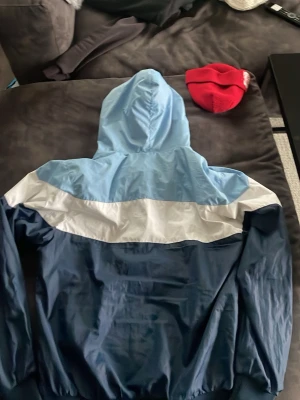 Malmö FF vindjacka i blått och vitt - Snygg vindjacka från Malmö FF i två nyanser av blått och vitt. Jackan har huva, dragkedja framtill och är perfekt för dig som vill visa ditt stöd för laget. Lätt och smidig att bära, passar till många tillfällen.