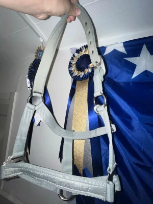 Ljusgrå grimma med text och stjärnor - Säljer en ljusgrå grimma i slitstarkt nylon med justerbart nackstycke och metallspännen. På nosdelen står det 'SUPER STAR' i vitt med små stjärnor. Passar perfekt till A-B ponny kanske C ponny beroende på huvud form.