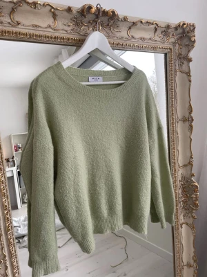 Grön stickad tröja från MSCH - Ljusgrön stickad tröja från MSCH Copenhagen med rund halsringning och avslappnad passform. Tröjan har ribbade muddar vid ärmslut och nederkant, vilket ger en snygg och enkel look. Perfekt för lager på lager och riktigt mysig.
