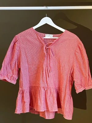 Röd- och vitrutig blus med volang - Söt blus i röd- och vitrutigt mönster. Modellen har korta puffärmar, volang nedtill och knytning vid halsen. Tillverkad i ett lätt och luftigt bomullstyg som passar perfekt till sommaren. Köpt på Holly & Whyte, använd en gång❣️🤍 