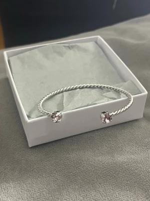 Caroline Svedbom armband  - Silver armband från Caroline Svedbom. Armbandet har en vriden design och är prydd med lila kristaller på ändarna. Lådan följer med. Använt 2 gånger. Pris kan diskuteras och kan ordna fri frakt 