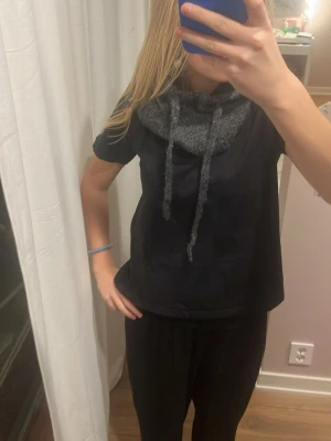 Mörkgrå stickad balaclava - Mysig mörkgrå stickad halsduk med huva och långa snören framtill. Perfekt att dra över huvudet för extra värme och stil. Passar till många olika outfits och är enkel att matcha. Materialet känns mjukt och värmande.denna är aldrig använd 