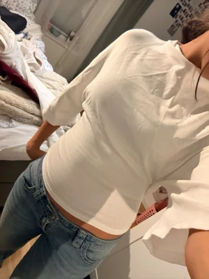 Vit omlottopp med knyt från Gina Tricot - Snygg vit omlottopp från Gina Tricot med croppad passform och knyt i ryggen. Toppen har halvlånga ärmar och en öppen rygg som ger en cool look. Tillverkad i mjukt bomullsmaterial som känns skönt mot huden. Perfekt att styla med  jeans eller kjol. 