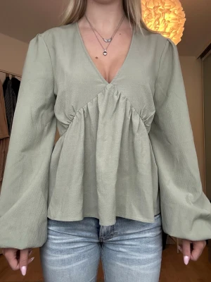 Ljusgrön blus med v-ringning från NA-KD - Supersöt ljusgrön blus från NA-KD med v-ringning och långa, vida ärmar. Blusen har en snygg rynkning under bysten.